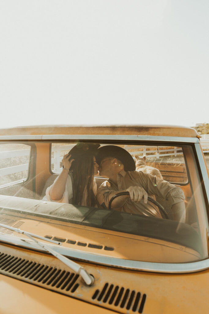 couple sits in their old ford truck wearing cowboy hats kissing